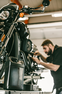Mechanic working on a motorcycle in a repair shop, focusing on engine maintenance with tools in hand.
