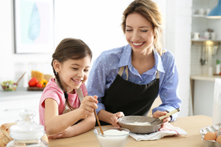 Mother and daughter happily baking together in a kitchen, mixing flour in a bowl.