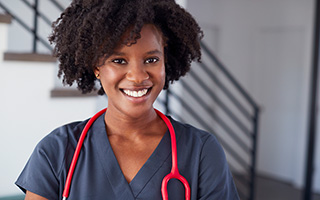Nurse in blue scrubs with a red stethoscope around her neck standing in an office setting.