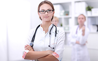 Nurse with glasses and a stethoscope n a hospital corridor with colleagues in the background