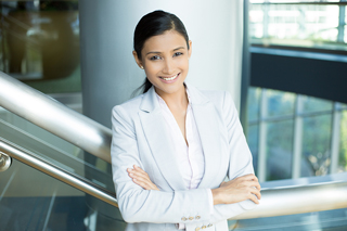 Confident businesswoman smiling in a light gray suit stands at an office railing.