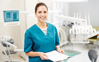 Female dental assistant in scrubs holding a clipboard in a modern dental office.
