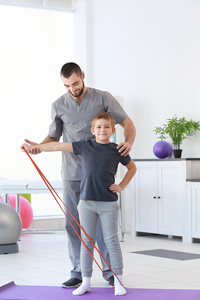 Young boy exercising with resistance band supervised by male physical therapist in a bright clinic room