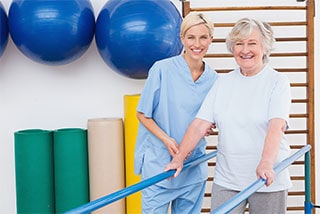 Physical therapist assisting elderly woman with leg exercise in clinic gym