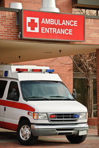 Ambulance parked at hospital entrance with prominent red cross and 'AMBULANCE ENTRANCE' sign visible.