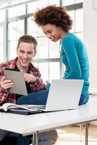 Two young professionals collaborating with a laptop and tablet in a bright office space