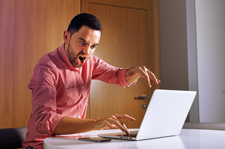 Man in pink shirt looking surprised while using laptop at an office desk