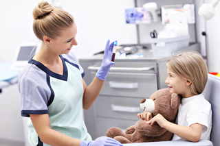Phlebotomist showing a young girl a smartphone in a clinic, child holding a teddy bear.