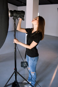 Photographer adjusting studio light for a photoshoot, wearing casual clothing in a professional photography studio.