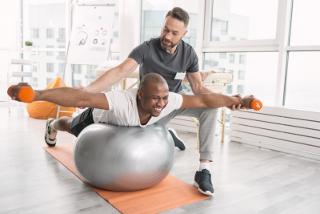 Physical therapist assisting patient with leg stretches on exercise ball in clinic