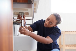 Plumber repairing sink pipe in kitchen.