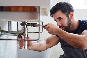 Plumber repairing a sink pipe with a wrench in a kitchen setting