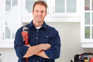 Plumber in blue uniform holding a red wrench in a modern kitchen setting
