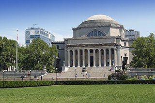 Columbia University's Low Memorial Library facade on a sunny day, featuring its iconic neoclassical architecture with columns and dome, surrounded by green lawns.