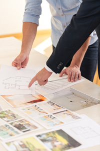Two property management professionals examining architectural blueprints and design plans on a table in an office setting.