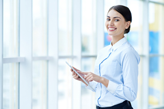 Professional woman in a blue shirt holding a tablet in a bright office environment