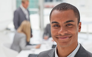 Real estate broker smiling at the camera in an office setting with colleagues in the background
