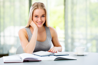 Young woman studying with books and coffee cup at modern table indoors