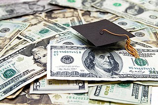 Graduation cap on a pile of US dollar bills, symbolizing the cost of education or student debt.