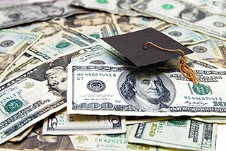 Graduation cap on a pile of US dollar bills, symbolizing the cost of education.