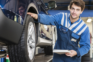 Young male mechanic inspecting car tire and taking notes in a workshop