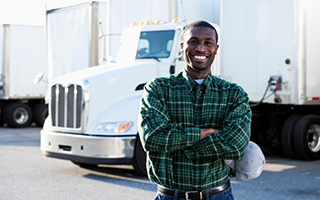 Smiling truck driver in plaid shirt standing in front of white semi-truck