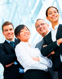 Four smiling business professionals with a blurred modern building background.