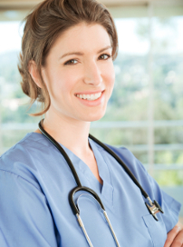 Nurse in blue scrubs with a stethoscope around her neck standing in a bright room.