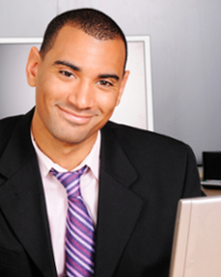 Businessman in office setting with computer, wearing a suit and striped tie.