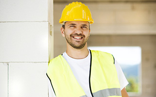Construction worker in yellow hard hat and reflective vest standing by a wall