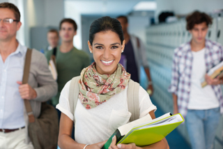 Smiling young female student with books walking in school hallway with other students in background