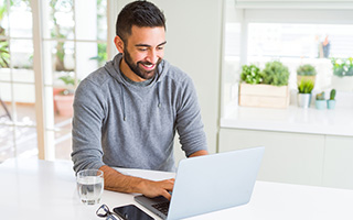 Man with beard smiling and using laptop at modern kitchen table