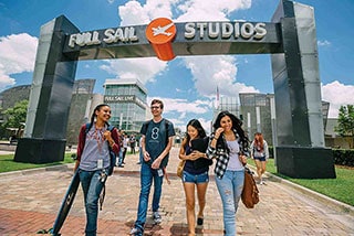 Group of diverse students walking under the Full Sail Studios archway on a sunny day.