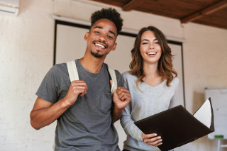 Two college students, a young man with a backpack and a young woman holding a laptop, happily walking in a well-lit room