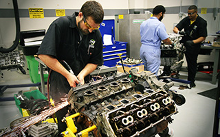 Mechanics working on car engines in an automotive workshop, one closely inspecting engine parts