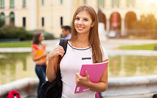 Smiling young female student with backpack holding books at university campus