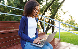 Young woman using laptop on park bench