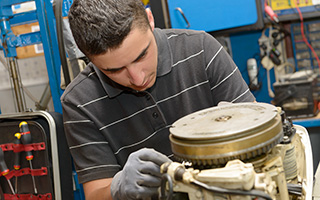 Mechanic in striped polo shirt working on a machinery component in a workshop with tools in background