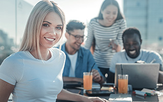 Young woman with colleagues working on laptop at outdoor cafe with city background