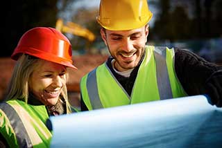 Two construction technicians wearing hard hats reviewing blueprints.