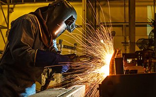 Welder in protective gear using welding machine in industrial environment, creating bright sparks