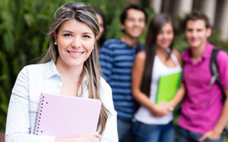 Female student holding notebooks with three classmates in background on university campus