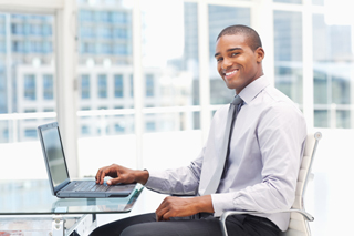 Businessman using laptop at office desk with cityscape in background