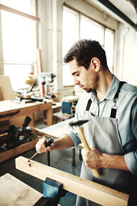Carpenter using a chisel and mallet on a piece of wood in a sunlit workshop
