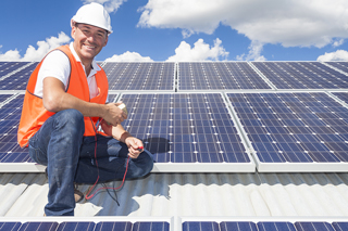 Solar energy technician in hard hat and safety vest installing solar panels on roof with sunny sky in background