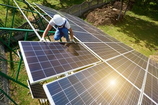 Solar power worker in hard hat installing solar panels on a sunny day