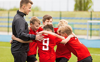 Young soccer players in red jerseys huddling around their coach on outdoor field