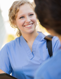 Sterile processing technician in blue scrubs talking to a colleague outdoors