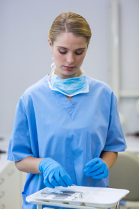 Scrub tech in blue scrubs and gloves preparing surgical instruments in a clinic