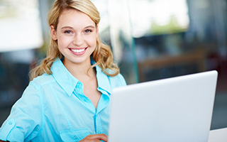 Smiling female student in a blue blouse working on her laptop